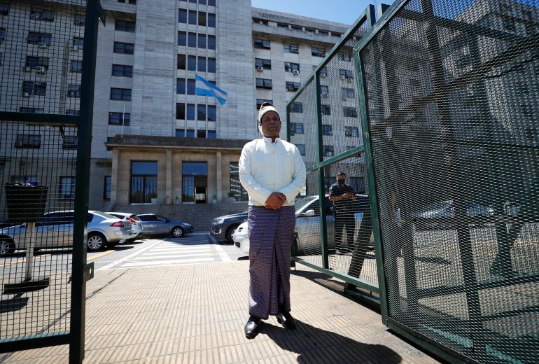 Rohingya activist Tun Khin, in traditional sarong and white shirt, stands at the gates of the Comodoro Py court in Buenos Aires, Argentina in December.