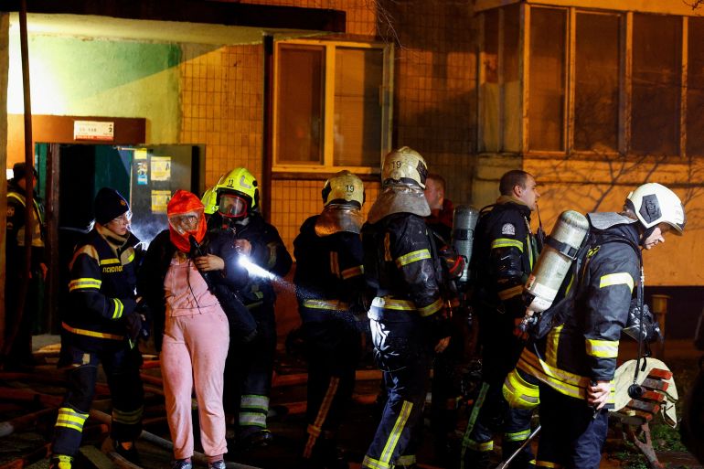 Firefighters assist a resident at the site of an apartment building hit in an attack.