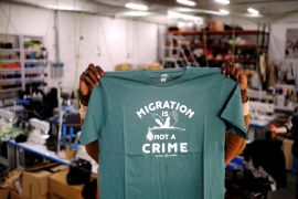 A person holds up a T-shirt with "Migration is not a crime" printed on it.
